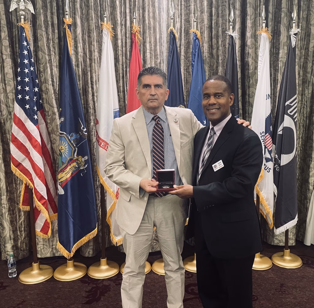 Former WDVA Secretary John Scocos presents WDVA Secretary James Bond a challenge coin